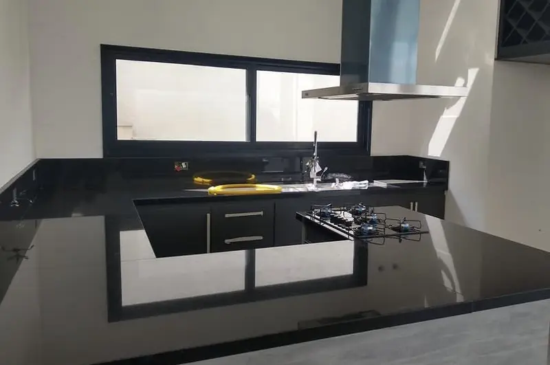 Cozinha com bancada em granito preto, cooktop e coifa