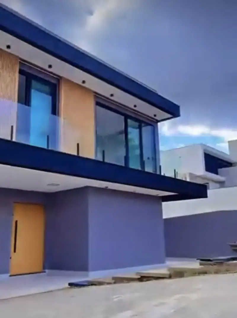Fachada de casa de dois pavimentos com guarda-corpo em vidro e porta em madeira