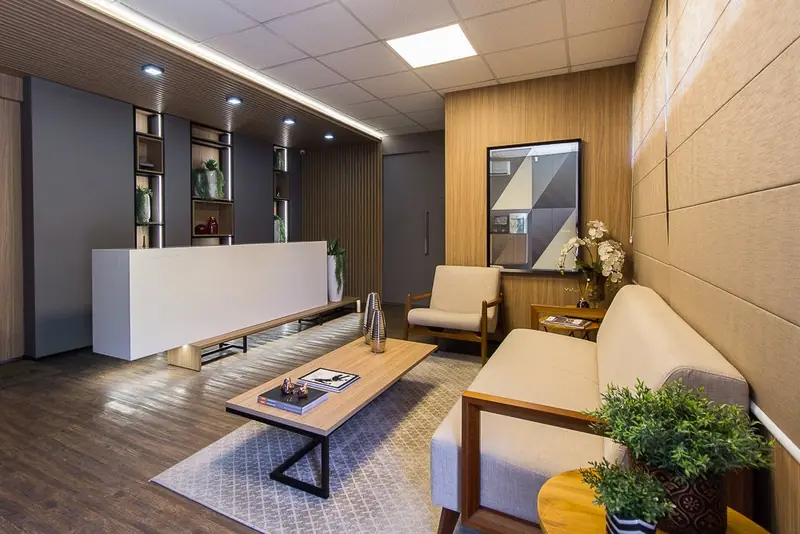 Recepção com balcão branco, painéis em madeira e sala de espera