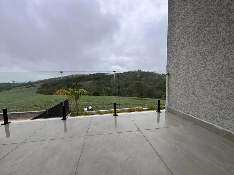 Varanda com guarda-corpo de vidro e vista para o campo