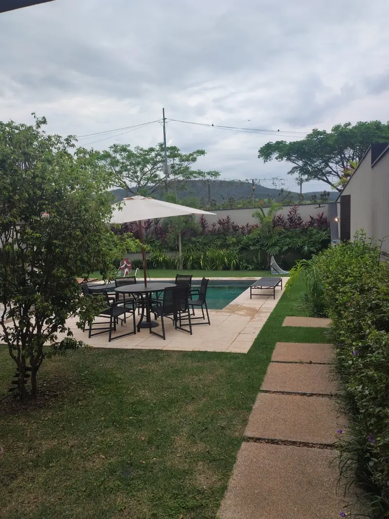 Jardim com mesa, guarda-sol e piscina ao fundo